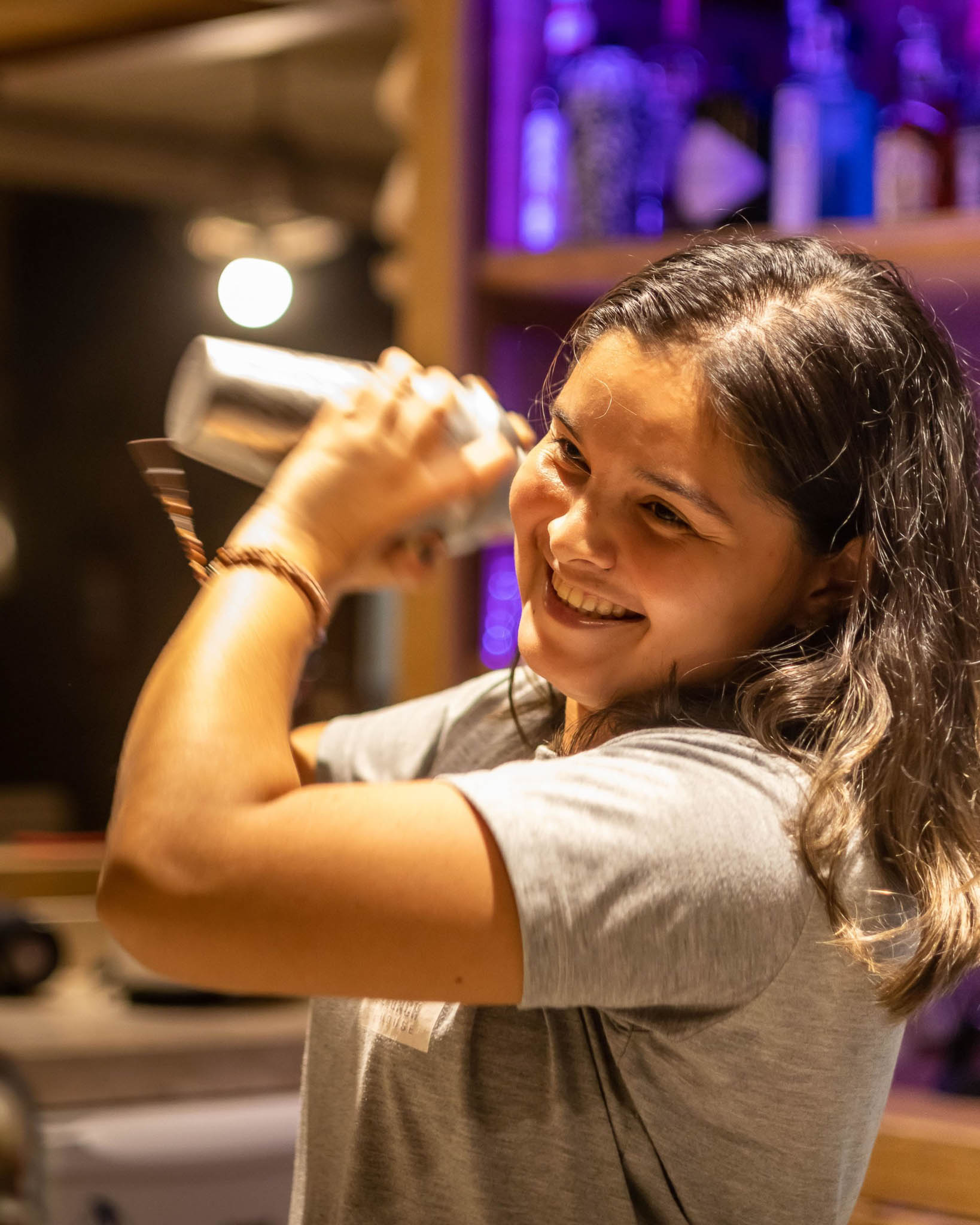 Barmaid souriante préparant un cocktail au shaker au bar de la OLK House, Pontal de Maceió